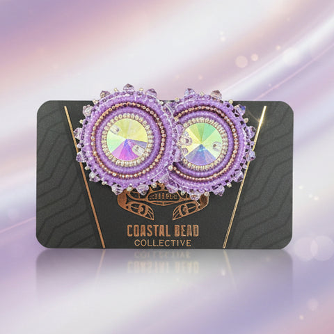 Decorative earrings on a black card with visible brand name, placed on a wooden surface.