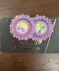 Decorative earrings on a black card with visible brand name, placed on a wooden surface.