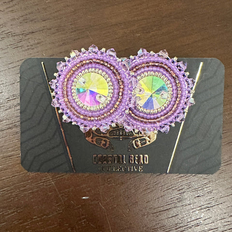 Decorative earrings on a black card with visible brand name, placed on a wooden surface.