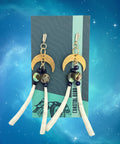 Pair of earrings with moon designs on a branded card, placed on a wooden surface.