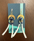 Pair of earrings with moon designs on a branded card, placed on a wooden surface.