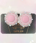 Pair of pink earrings with pearl details on a dark card against a wooden surface