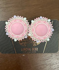 Pair of pink earrings with pearl details on a dark card against a wooden surface