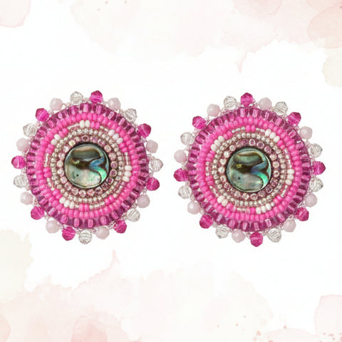 Pair of pink earrings on a card with 'Coast Collection' branding on a wooden surface.