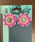 Pair of pink earrings on a card with 'Coast Collection' branding on a wooden surface.