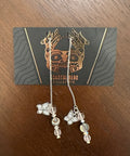 Pair of earrings on a card with a decorative design, placed on a wooden surface.