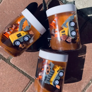 Three clear containers with toy construction vehicles on a textured surface