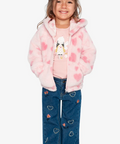 A young girl smiling and wearing a pink fuzzy hooded jacket with heart patterns, a pink graphic t-shirt, blue jeans with heart embroidery, and white sneakers, set against a plain light gray background.