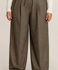 A person wearing wide-leg pleated trousers in a muted taupe-brown color, styled with a cream ribbed long-sleeve top and dark brown shoes, against a plain light beige studio background.
