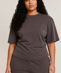 A woman modeling a matching dark brown lounge set consisting of a short-sleeve crewneck t-shirt and coordinating sweatpants, photographed against a solid light beige background.