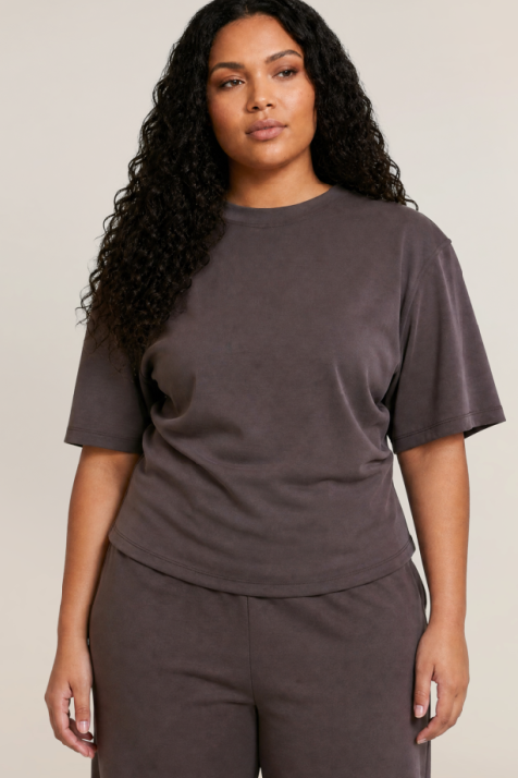 A woman modeling a matching dark brown lounge set consisting of a short-sleeve crewneck t-shirt and coordinating sweatpants, photographed against a solid light beige background.