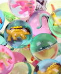 A close-up pile of colorful translucent glass toy balls, each containing a small dinosaur or reptile figure, photographed against a bright white background.