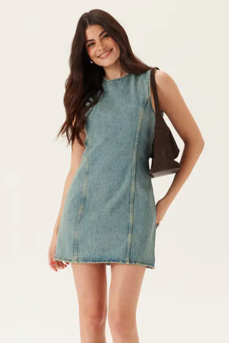 Woman wearing a denim dress holding a brown handbag on a white background