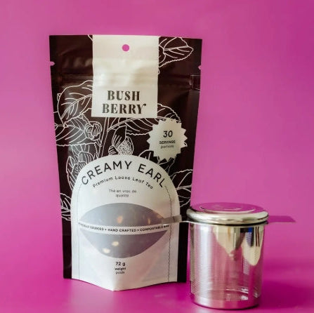 Tea package labeled 'Bush Berry Creamy Earl' with a metal tea container on a pink background