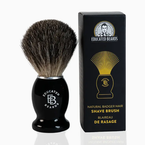 Shave brush with black handle and bristles next to its packaging on a white background