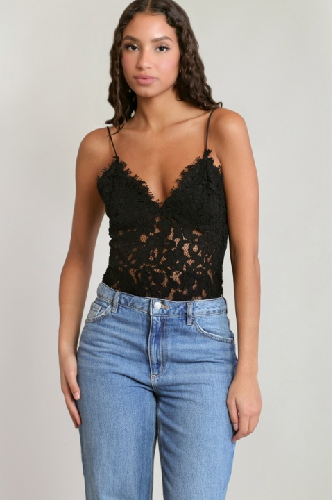A woman modeling a black lace camisole top with thin straps and blue jeans against a plain light gray studio background.