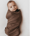 Baby wrapped in a brown swaddle on a white background