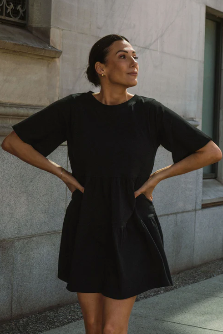 Woman wearing a black dress standing against a stone building.