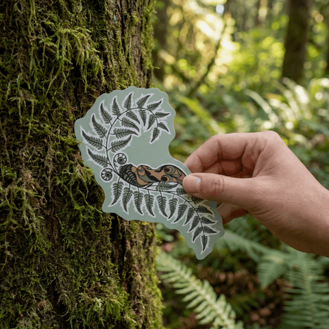 Hand holding a nature-themed sticker against a forest background