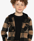 A young boy with curly brown hair and freckles wearing a brown and black buffalo plaid hooded flannel shirt over a black t-shirt, photographed against a solid light gray background.