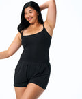 A woman modeling a black two-piece activewear set consisting of a scoop-neck tank top and matching high-waisted shorts, posed against a solid white background.