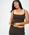 A woman wearing a matching dark brown activewear set consisting of a spaghetti-strap tank top and athletic shorts, posing against a light gray studio background.