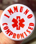 Button badge with 'IMMUNOCOMPROMISED' text and red medical symbol held by a hand.