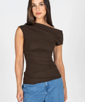 A woman modeling a dark brown off-the-shoulder short-sleeve top with ruched detailing, paired with blue jeans, against a plain light gray background.