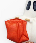 A close-up of a white ghost-shaped product, likely a cupcake topper or decorative figurine, holding a red gift bag. The ghost has black eyes and metallic gold accents on its hands and feet, set against a plain white background.