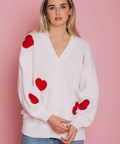 Woman wearing a white sweater with red heart patterns against a pink background