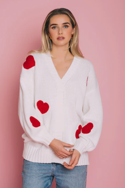 Woman wearing a white sweater with red heart patterns against a pink background
