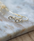Gold earrings with teardrop-shaped gemstones on a marble surface
