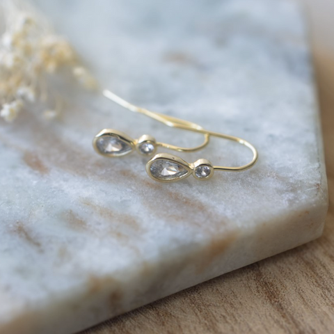 Gold earrings with teardrop-shaped gemstones on a marble surface