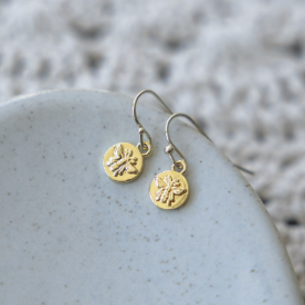 Gold earrings with circular designs on a textured stone surface