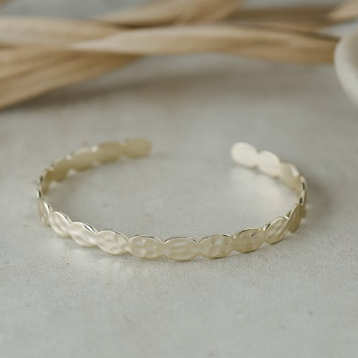 Gold bracelet on a light gray surface with dried plants in the background