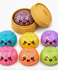 A set of seven colorful glittery squishy buns with cute cartoon faces, displayed next to a round wooden box containing one bun filled with multicolor glitter. The buns are in various colors: blue, yellow, purple, pink, orange, green, and a mix of glitter.