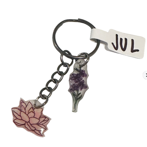 Keychain with floral charms and 'JUL' tag on a textured surface