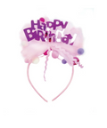 A pink headband with a decorative 'Happy Birthday' party accessory, featuring purple lettering, pink tulle, pom-poms, and a curly ribbon on a white background.