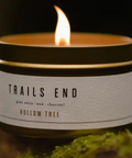 Candle in a container labeled 'Trails End Hollow Tree' on a dark background