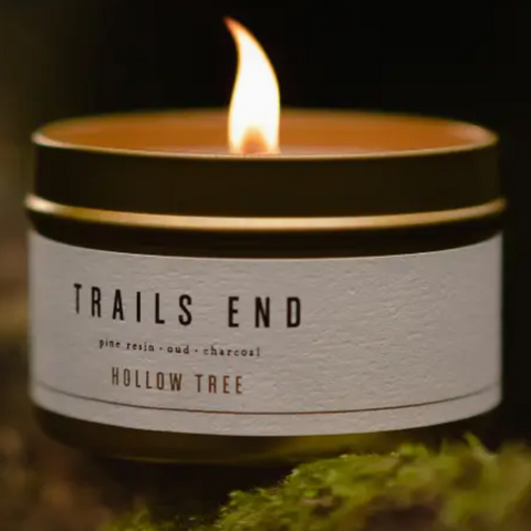 Candle in a container labeled 'Trails End Hollow Tree' on a dark background