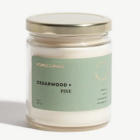 Candle jar labeled 'Homecoming Cedarwood + Pine' on a white background