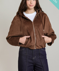 A woman modeling a brown zip-up hooded jacket with a fuzzy texture, worn over a white t-shirt and dark blue jeans, against a light gray background with a teal 'BEST SELLERS' banner in the top right corner.