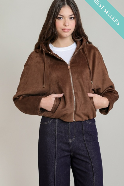 A woman modeling a brown zip-up hooded jacket with a fuzzy texture, worn over a white t-shirt and dark blue jeans, against a light gray background with a teal 'BEST SELLERS' banner in the top right corner.