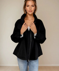 Woman wearing a black coat and light blue jeans against a plain background