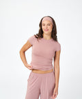 A woman modeling a matching dusty pink activewear set consisting of a short-sleeve crop top, matching pants, and a matching headband, set against a plain white studio background.