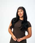 A woman with long black hair wearing a dark brown athletic short-sleeve top and matching headband, posing against a solid white studio background.