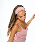 A woman wearing a dusty pink athletic headband and matching pink sports bra, posing against a solid white background.