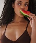Woman eating a watermelon slice wearing a brown bra.
