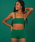 Woman wearing a green sports bra and shorts set against a green background