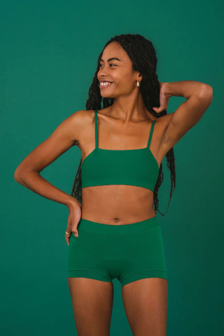 Woman wearing a green sports bra and shorts set against a green background